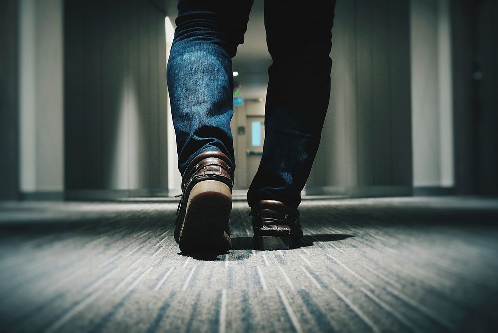 A low shot of a person in jeans walking through a hotel corridor. Original public domain image from Wikimedia Commons