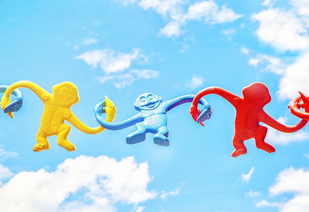 Yellow, blue and red plastic monkeys holding their hands against a blue sky. Original public domain image from Wikimedia…