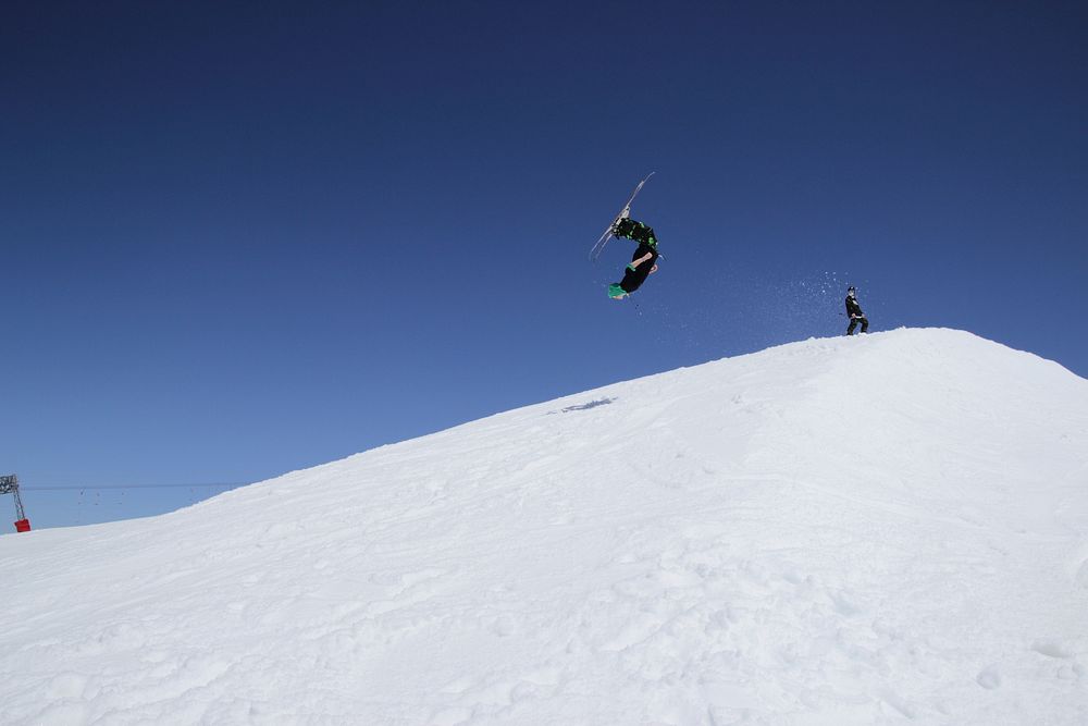 A skier upside down mid-flip over a snowy hill against a clear, blue sky. Original public domain image from Wikimedia Commons