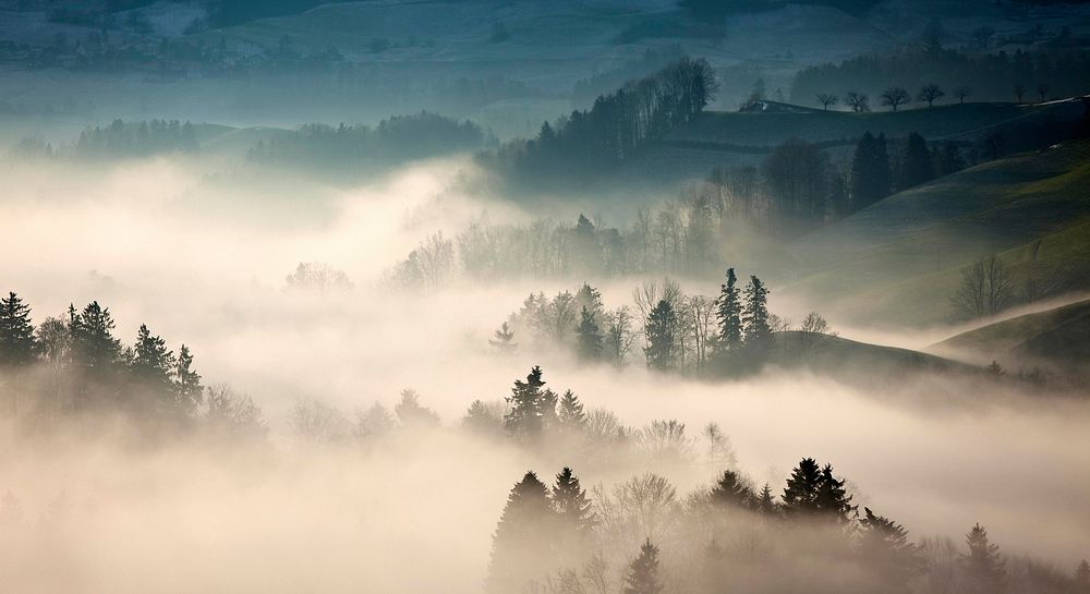 A hilly rural landscape wreathed in a dense fog. Original public domain image from Wikimedia Commons