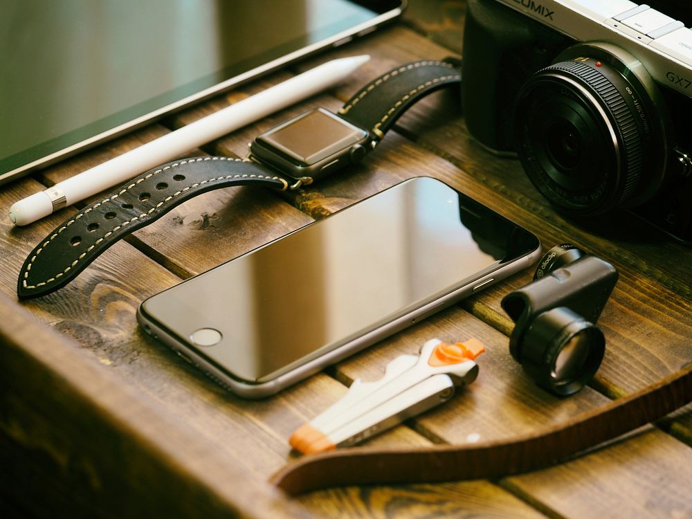 An iPhone, an Apple Watch and a digital camera on a wooden surface. Original public domain image from Wikimedia Commons