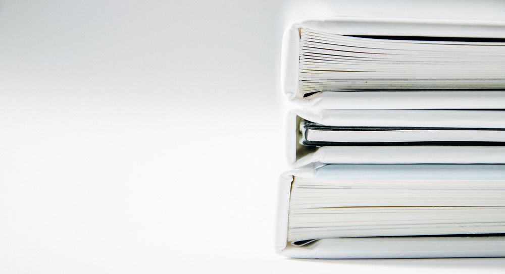 A stack of thick folders on a white surface. Original public domain image from Wikimedia Commons
