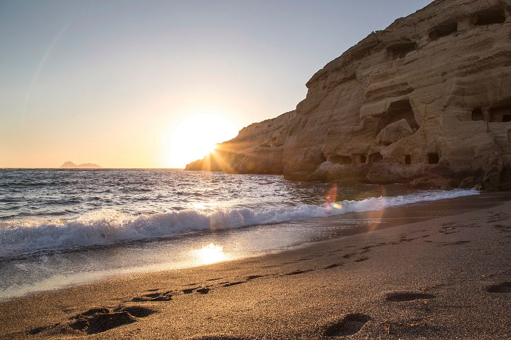 Sandy cliff beach under sunset. with foot marks along the shoreline leading toward a large rock coastline.