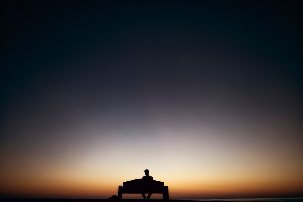 Sunset silhouette of a man sitting on bench alone in San Diego. Original public domain image from Wikimedia Commons