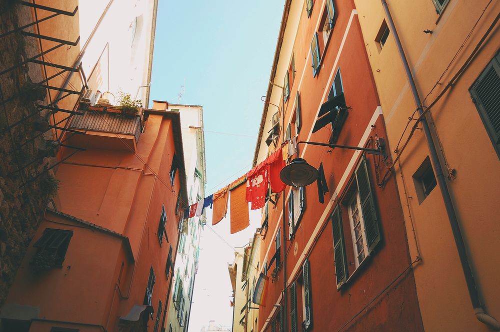 Wet clothes hanging on a line between two residential buildings in an alley in Genoa. Original public domain image from…