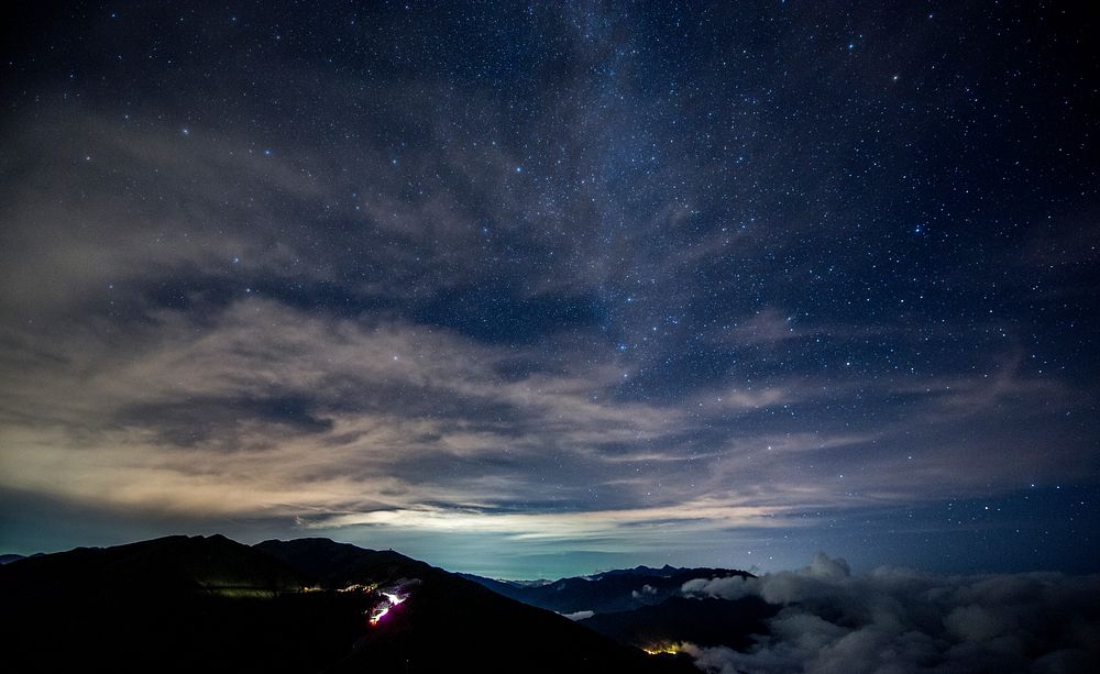 Stars twinkling through a cloudy sky over mountains. Original public domain image from Wikimedia Commons