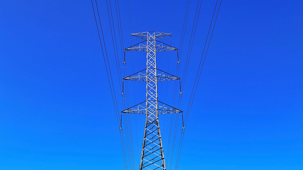 Electric tower with power lines creates symmetrical views on a clear blue sky. Original public domain image from Wikimedia…