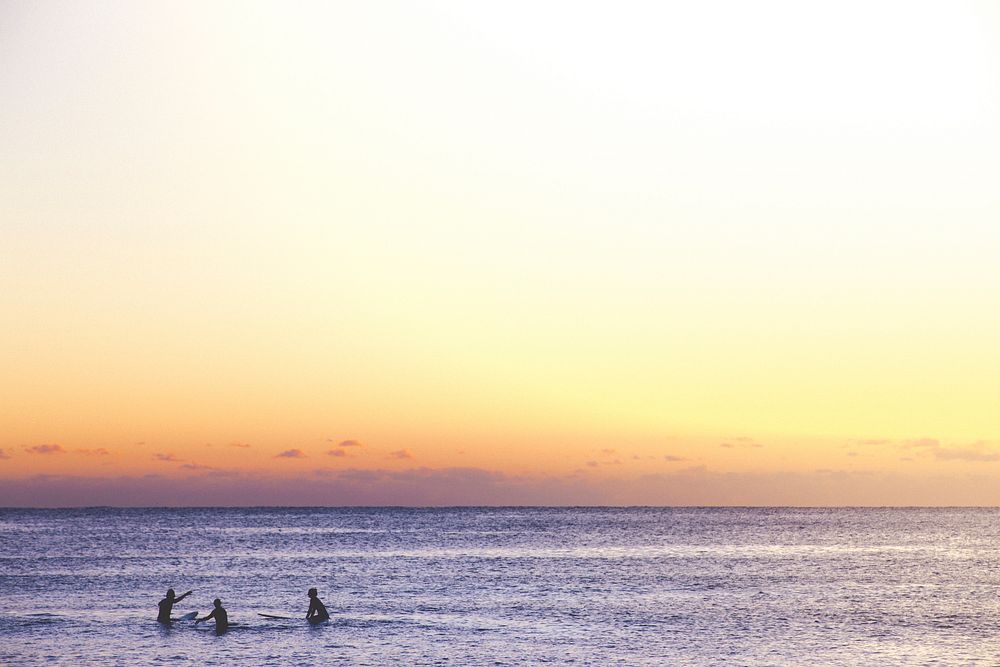 3 people in the calm, shallow sea at Sydney Beach, beneath a beautiful orange and purple sunset sky. Original public domain…