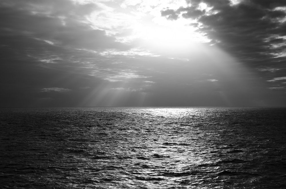 Black and white shot of sea with cloudy sky and sunrays coming through clouds. Original public domain image from Wikimedia…