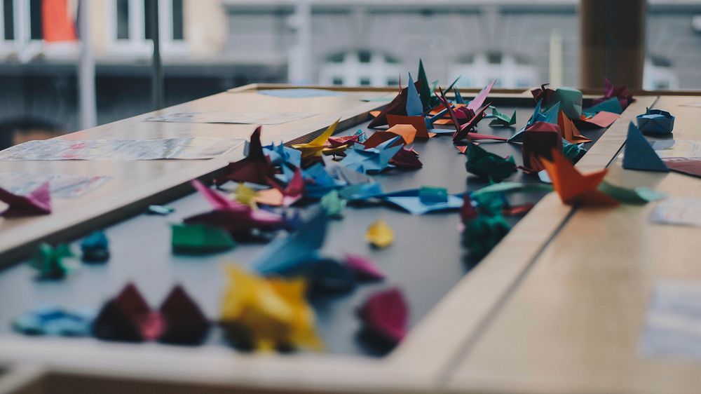 A large number of colorful origami cranes scattered across a table. Original public domain image from Wikimedia Commons