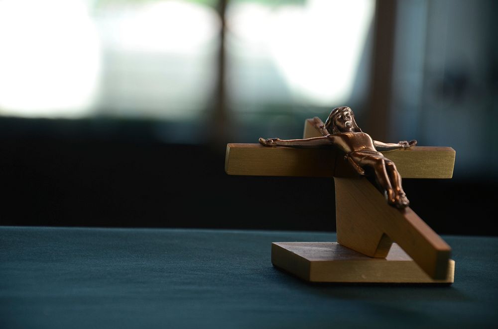 Wooden crucifix with figure of Jesus laying on a dark table. Original public domain image from Wikimedia Commons
