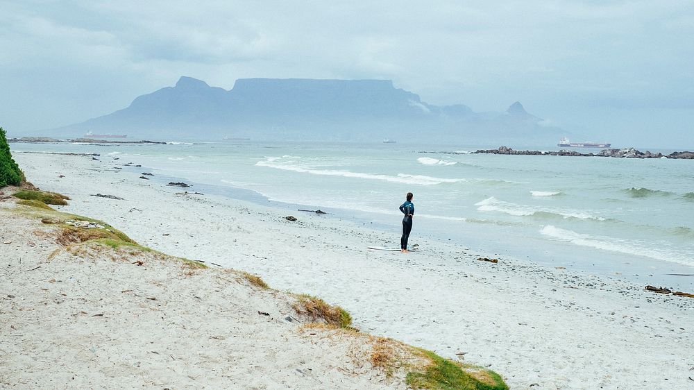 Woman surfer standing on the beach in Table View looking at the ocean. Original public domain image from Wikimedia Commons