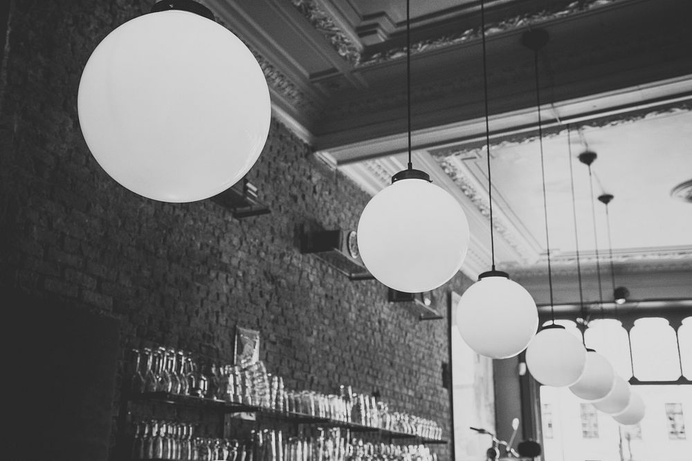 Black and white shot of cafe interior with brick wall and large lightbulbs hanging from ceiling. Original public domain…