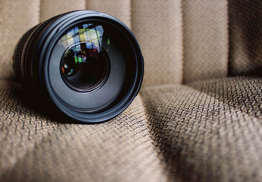 A close-up of a camera lens resting on the fabric texture of a chair.. Original public domain image from Wikimedia Commons