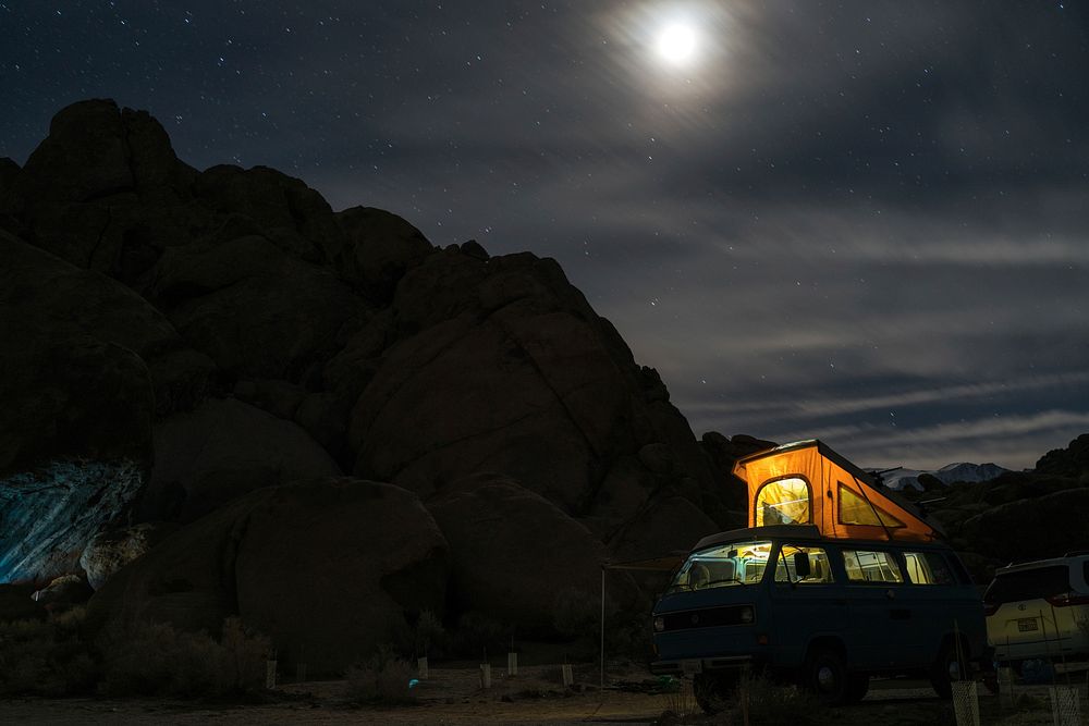 A camper van lit up at night under a full moon on a mountain.Original public domain image from Wikimedia Commons