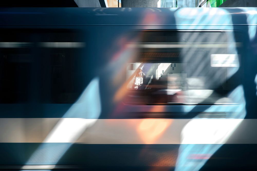 A blue train car blurring past briefly framing a person waiting. Original public domain image from Wikimedia Commons