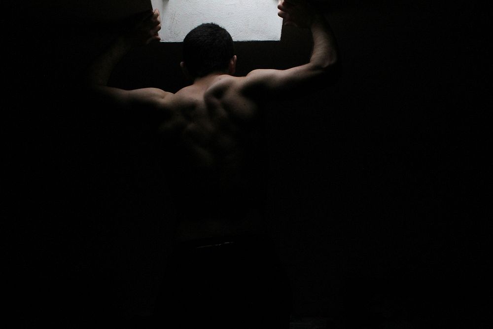 A dark image from behind a shirtless man. Original public domain image from Wikimedia Commons