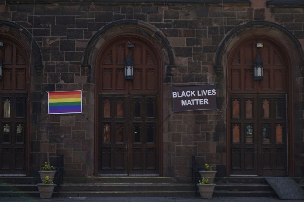 A rainbow flag and a flag writting "Black Lives Matter" hanged on the wall of a church together.. Original public domain…