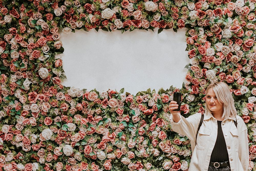 Woman taking a selfie by the flower wall installation with blank space 