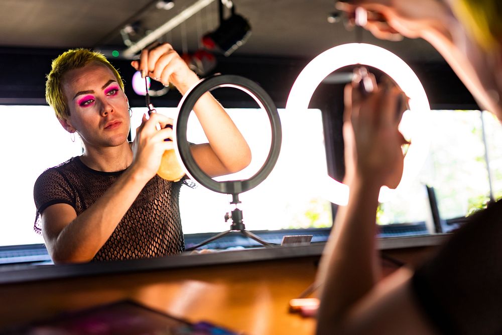 Non-binary person applying eye makeup, using LED ring light, beauty blogger