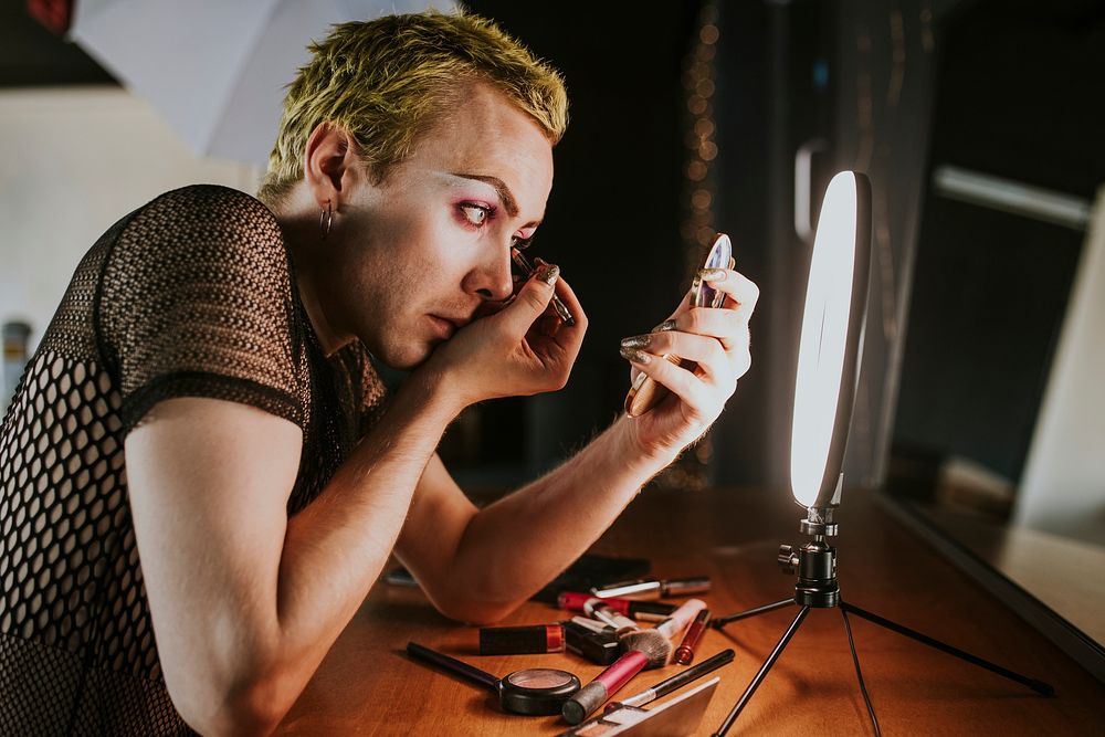 Non-binary person applying eye makeup, using LED ring light, beauty blogger