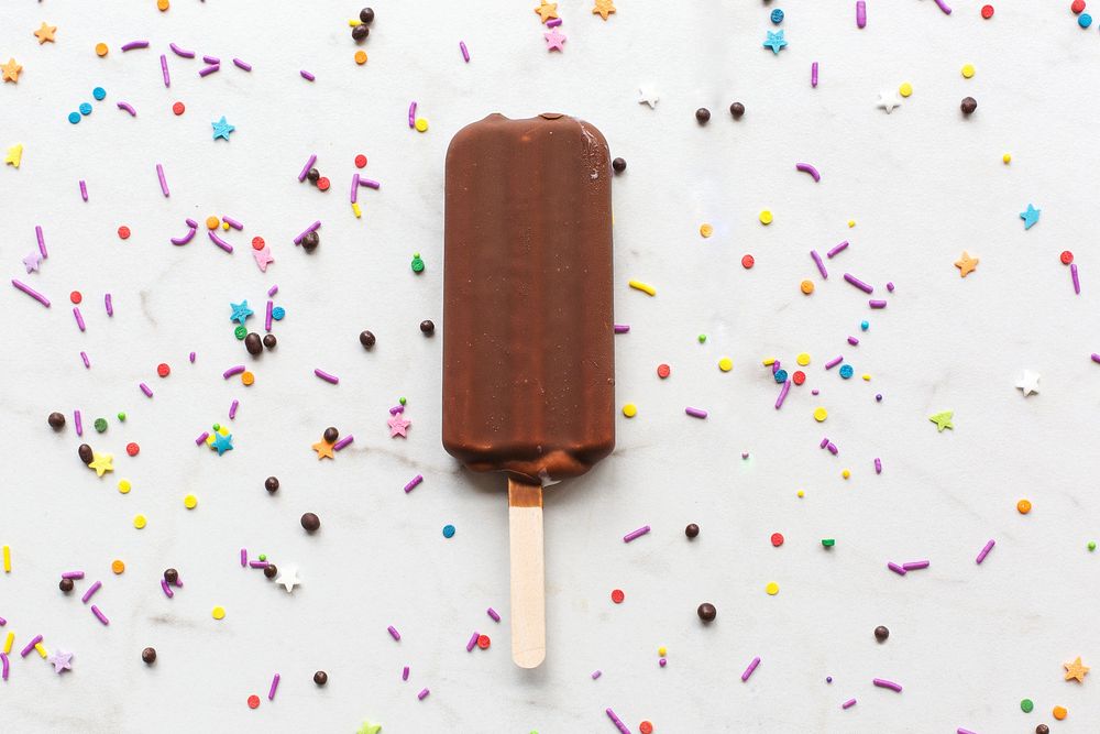 Chocolate covered ice cream bar on marble with sprinkles, free public domain CC0 image.