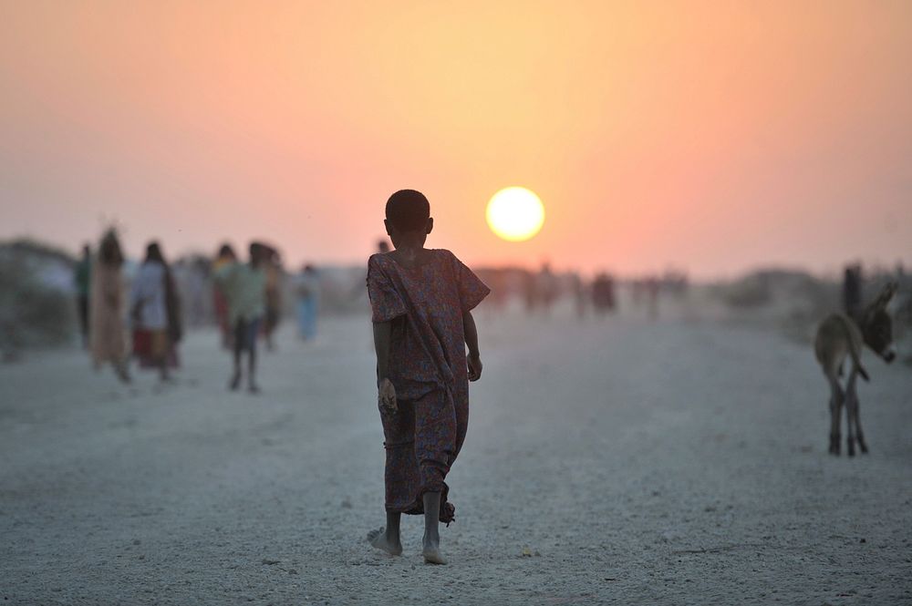 A Somali girl walks down a road at sunset in an IDP camp near the town of Jowhar. Original public domain image from Flickr