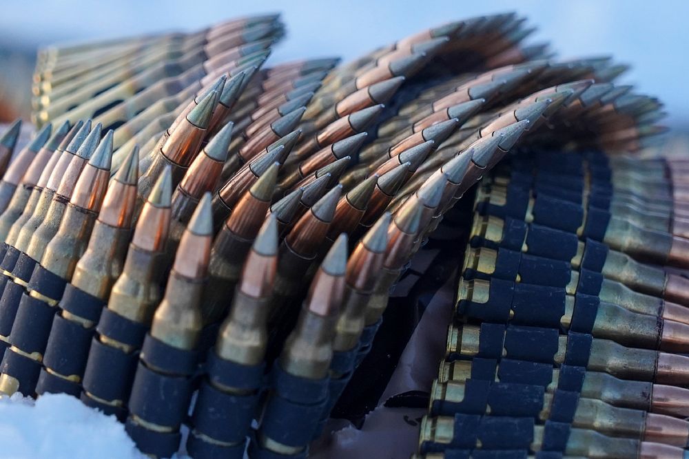 Linked belts of 7.62mm ammunition lays coiled on the ground as paratroopers assigned to the 2nd Battalion, 377th Parachute…