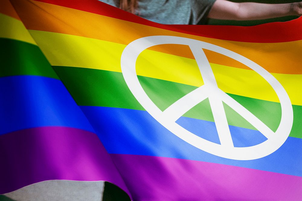 Person waving rainbow flag with peace sign, LGBTQ pride