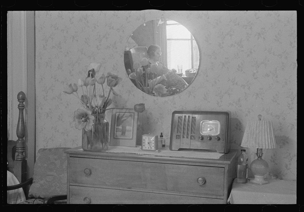 Washington, D.C. A corner of a bedroom, probably in a rooming house for government clerks, showing reflected in a round…