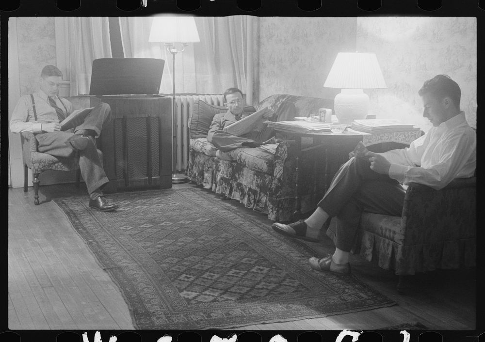 Washington, D.C. The room of a government clerk(?), showing three young men reading and listening to a radio in the evening.…