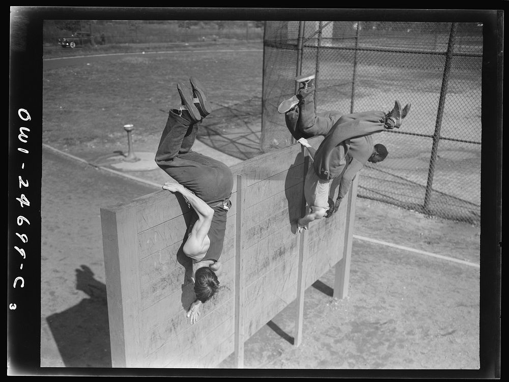 Flushing High School, Queens, New York, New York. Scaling an eight foot obstacle at top speed, part of the "commando"…