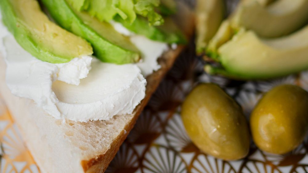 Healthy avocado toast serves on a modern patterned plate with olives closeup