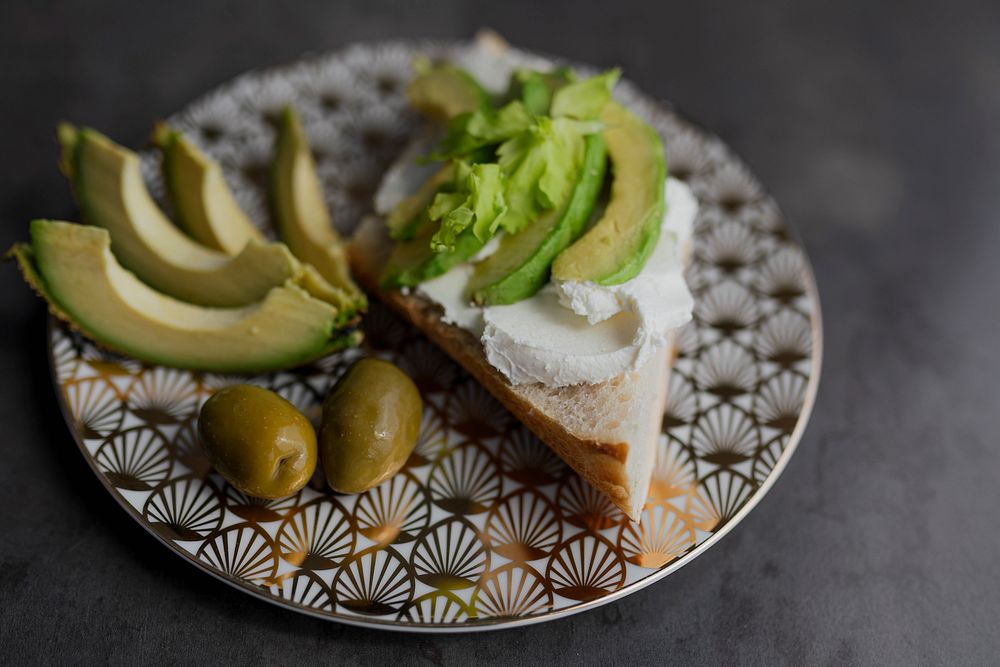 Healthy avocado toast serves on a modern patterned plate with olives