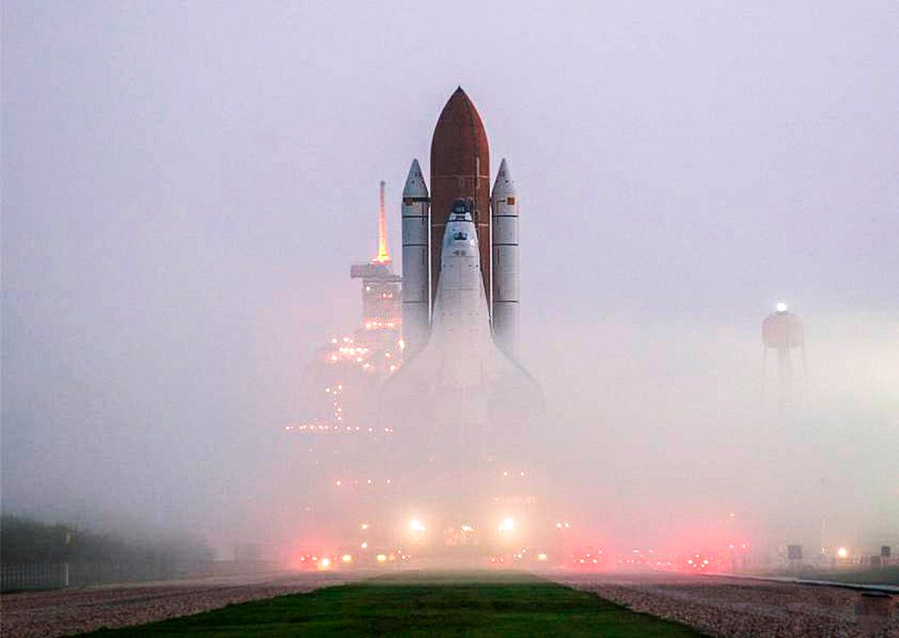KENNEDY SPACE CENTER, FLA. the fog on Launch Pad 39B is pierced by lights on vehicles and the service structures as Space…