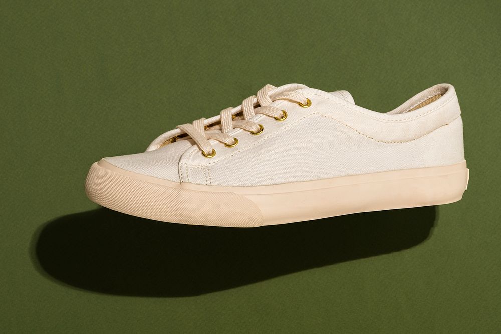 Unisex cream colored sneakers on an olive green background 