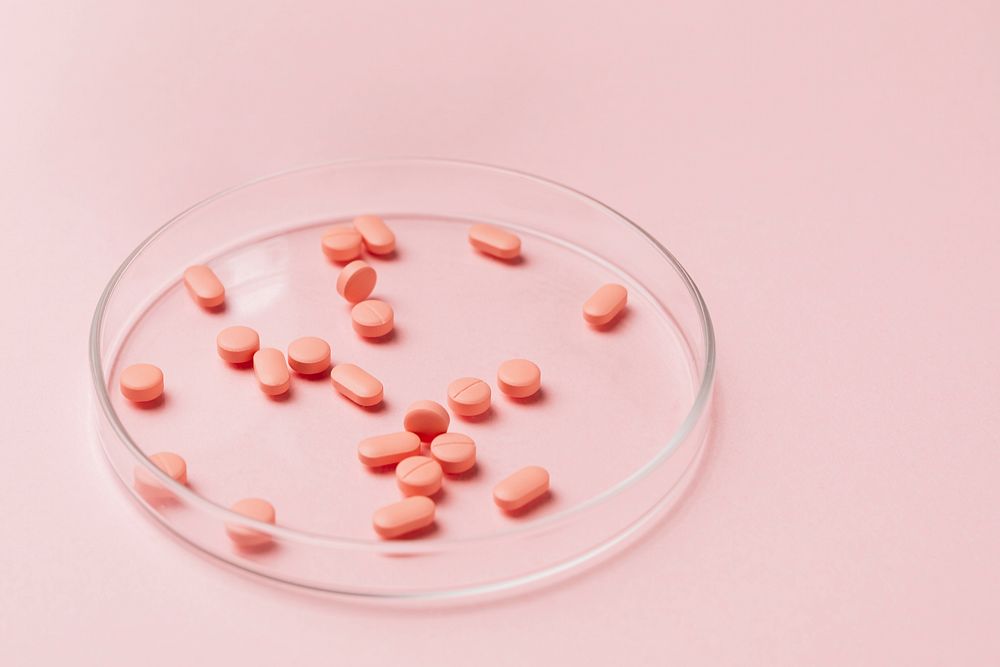 Pink pills on glass plate on pink background