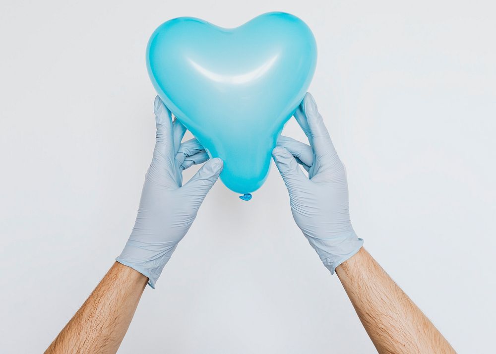 Gloved hands holding a blue heart shaped balloon  on a gray background