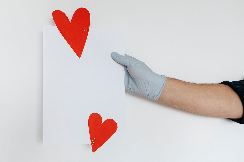Gloved hands holding a white card decorated with red hearts