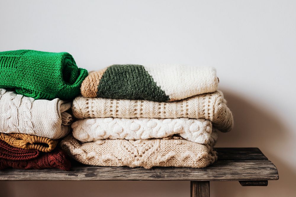 Folded winter sweaters on a wooden shelf 