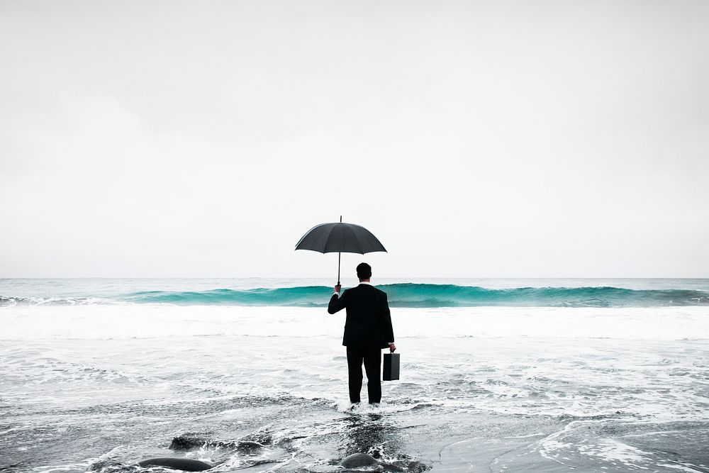Businessman in suit with umbrella standing in sea