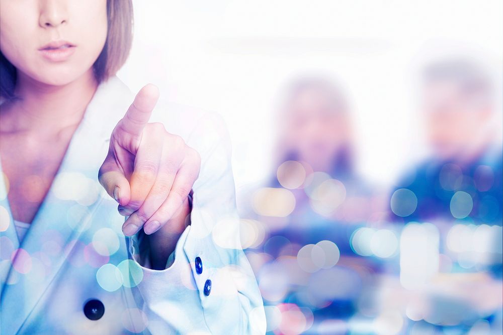 Young businesswoman in suit pointing on invisible screen with team background