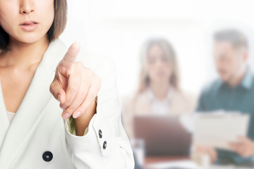 Young businesswoman pointing on invisible screen with team background