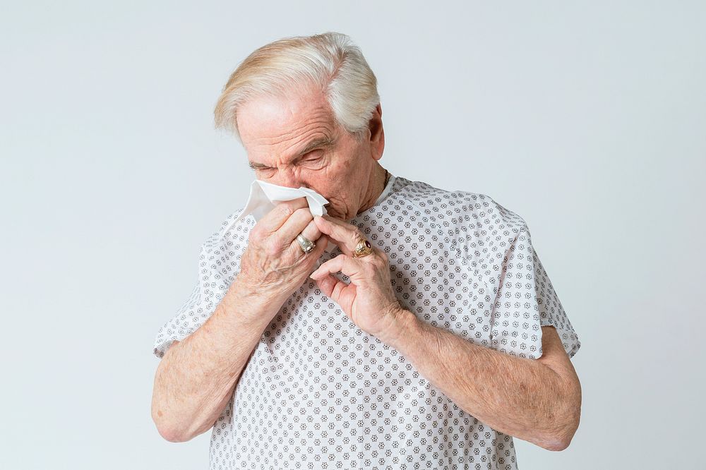 Coronavirus infected senior rman blowing nose into a tissue paper