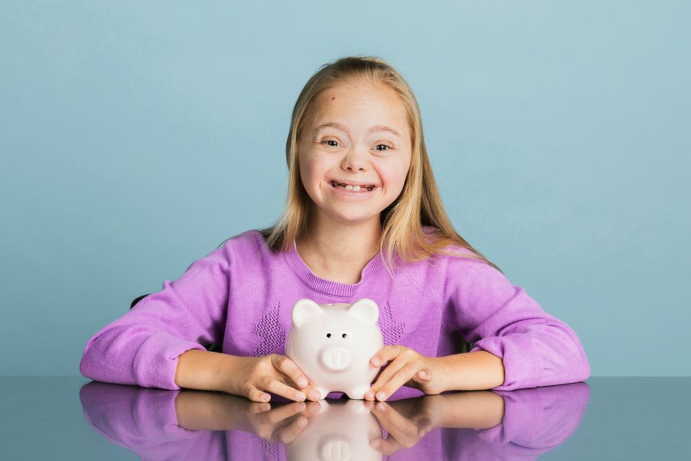 Cute little girl with Down Syndrome saving money in a piggy bank