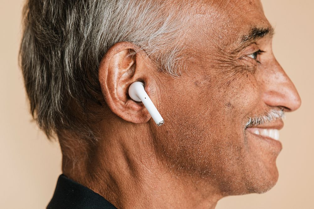 Senior Indian man listening to music with wireless earphones 