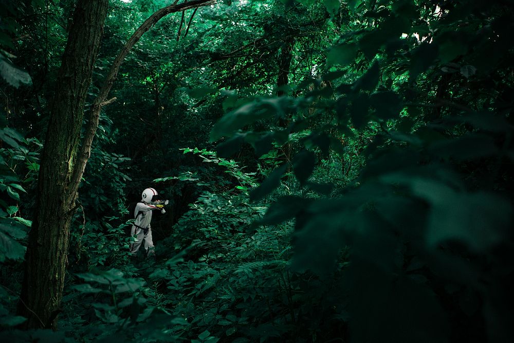 A person dressed in an other-worldly space suit surrounded by verdant forest vegetation on Nun's Island. Original public…