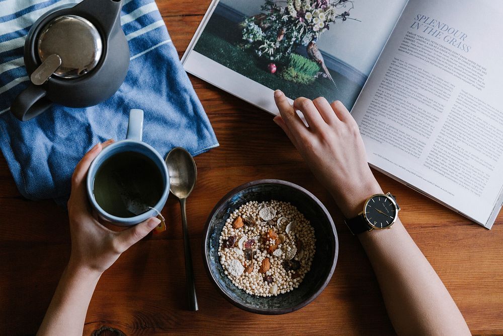 A person reading a book over a cup of coffee and a bowl of granola. Original public domain image from Wikimedia Commons