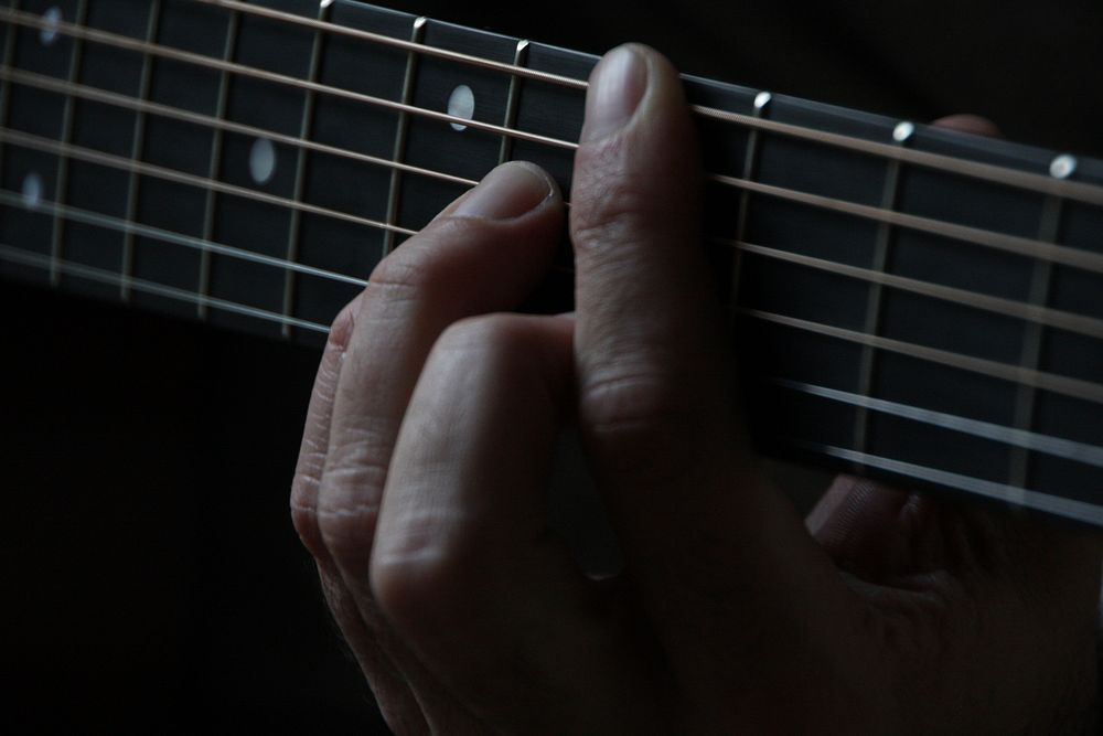 A close-up of a person's hands on the neck of a guitar. Original public domain image from Wikimedia Commons
