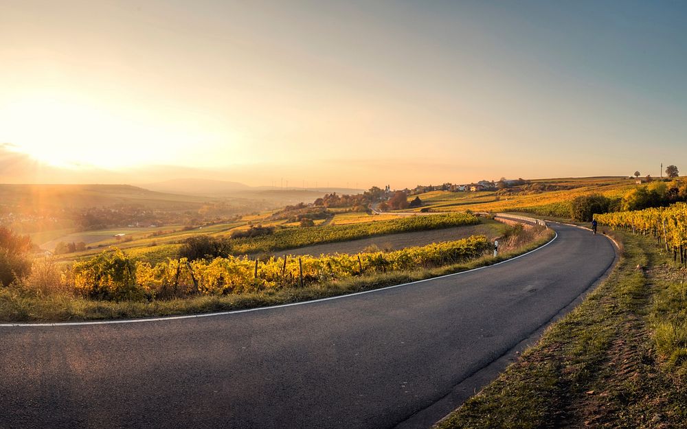 A sunset shines upon a winding asphalt road in Mölsheim, Germany and the many fields surrounding it. Original public domain…